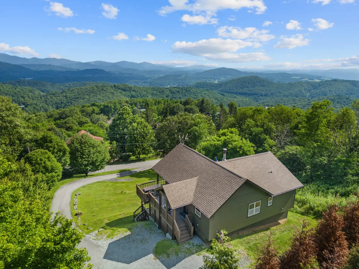 A stunning exterior shot of the house set among lush trees with dramatic mountains rising in the background. The deck offers a sweeping view, showcasing the serene, natural environment perfect for work and relaxation.