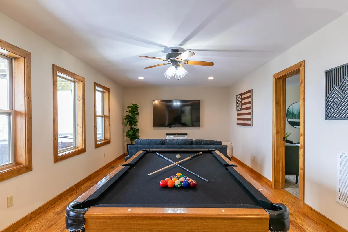 A casual and friendly recreation space with a pool table, large sofa, television, big windows, and decorative art. The area feels inviting, perfect for social gatherings and entertainment.