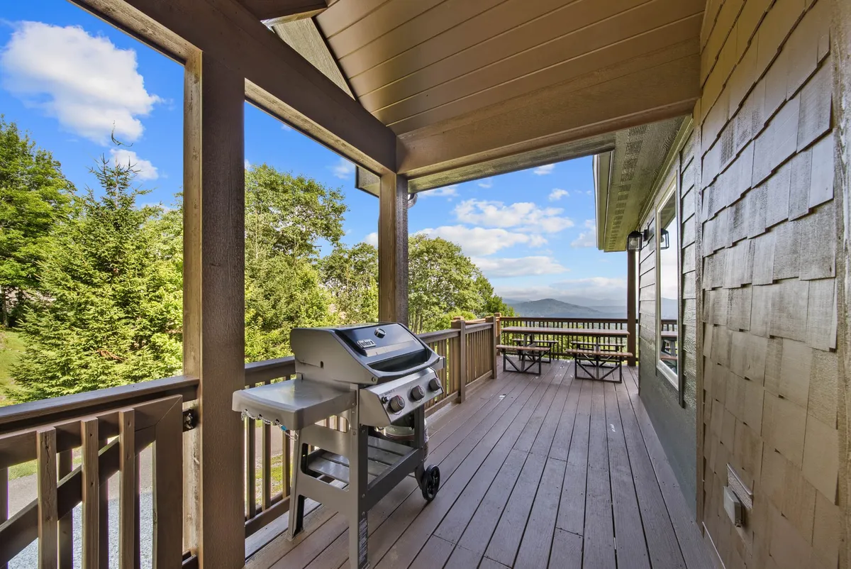 This image captures a main level wooden deck furnished with a grill and comfortable seating, overlooking a spectacular mountain view. The deck is spacious and highlights both the alfresco dining possibilities and the scenic backdrop. The railing and furniture suggest a private and inviting space perfect for relaxation or gatherings.