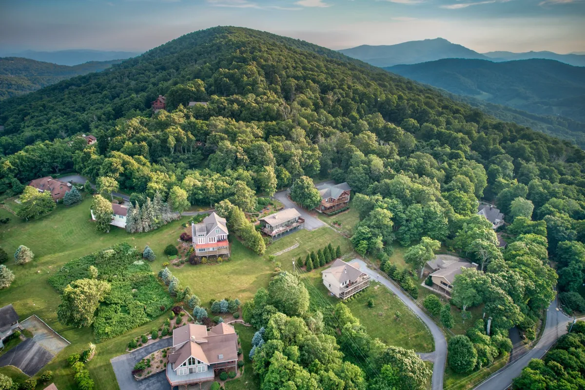 A broad, elevated view of rolling hills, wooded areas, and nearby homes, capturing the tranquil neighborhood straddling Boone and Blowing Rock. The natural landscape dominates, with hints of trails and open spaces that invite hiking and outdoor exploration.