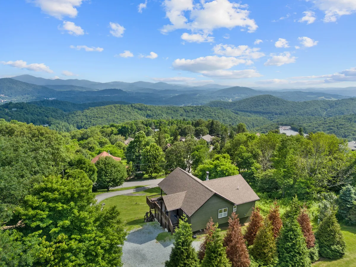 This image showcases Aussies Lookout nestled amidst lush greenery with a sweeping view of the surrounding mountain range. The tranquil exterior scene includes inviting areas for relaxing on the porch, and hints at the proximity to nature trails and outdoor adventure.