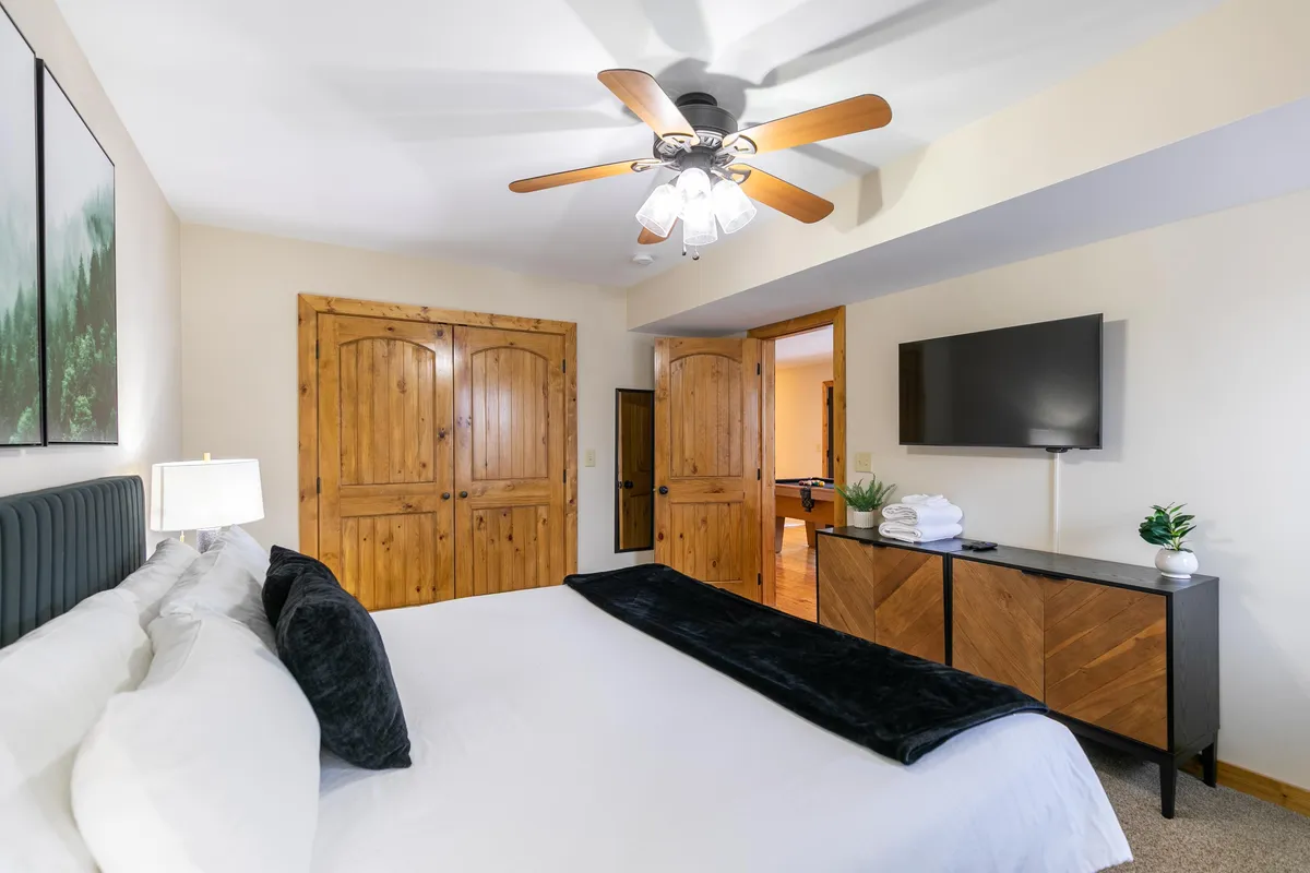 A cozy King bedroom featuring plush bedding, wooden closet doors, and a wall-mounted TV. The space is accented by soft lighting and a serene atmosphere, creating a setting for relaxation and comfort.