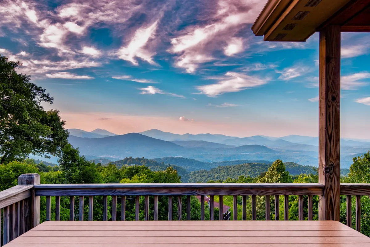 A wide view from the wooden deck overlooks a mountainous landscape beneath a colorful sky. The image captures sunset hues, with outdoor seating suggesting family gatherings, sunset watching, and stargazing opportunities after a day exploring the region.