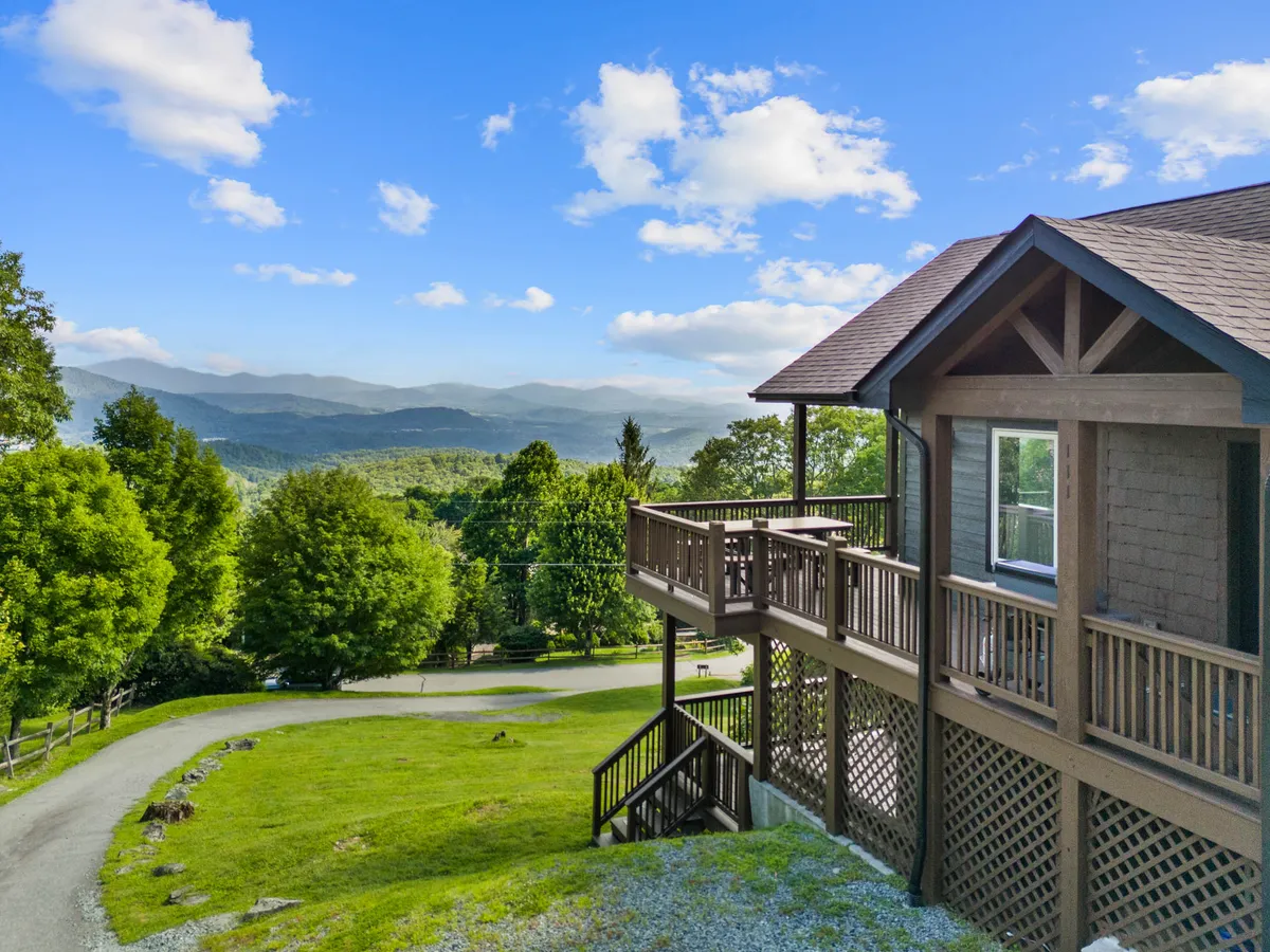 The hero image showcases a stunning wooden deck perched on a mountaintop, offering sweeping, unobstructed views of the Blue Ridge Mountains. The spacious deck invites guests to relax outdoors, with plenty of room for gathering, enjoying coffee at sunrise, or watching vibrant sunsets. The peaceful, natural surroundings and the expansive mountain vistas are front and center, creating a sense of tranquility and escape.