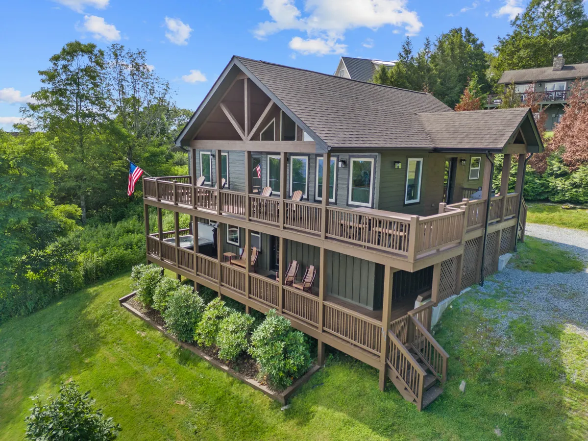 The photo showcases a balcony with comfortable chairs, an American flag, and abundant surrounding greenery. The deck is fully gated, offering a safe and tranquil space for pets and people to enjoy the outdoors together. The seating area suggests a place to unwind and gaze out at the mountain scenery.