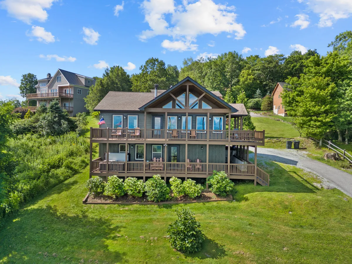This exterior image features a large deck bordered by secure railings, surrounded by lush greenery and panoramic windows that reflect the mountain landscape. The spacious deck is outfitted for gatherings and offers ample room for pets to enjoy the outdoors safely while owners take in the tranquil setting.