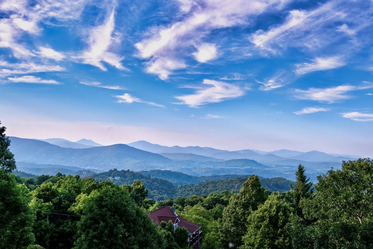 A wide-angle view capturing a majestic mountain range framed by verdant greenery and an expansive sky. The atmosphere is tranquil, evoking opportunities for sunrise viewing, stargazing, and quiet reflection.