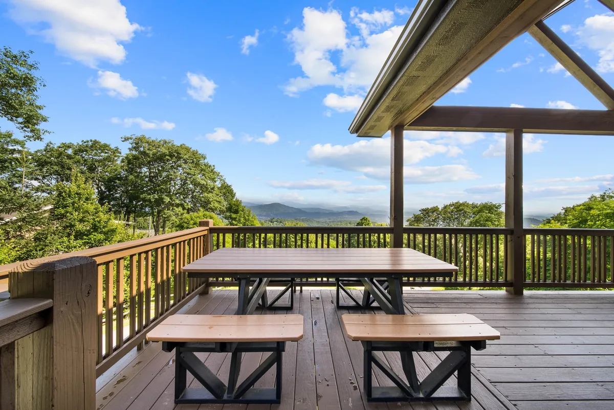 A wooden deck with a picnic-style dining table set against a stunning mountain backdrop, surrounded by trees. The space is ideal for group meals or morning coffee in the fresh air, underlining comfort and a seamless connection to nature.